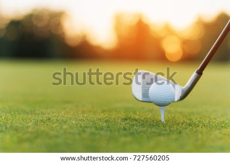 Close up. Stylish metal golf club and golf ball on a stand, against a sunset background. Low angle