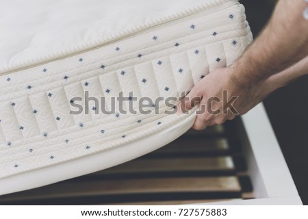 Close up. The man lifted the mattress to look at the bed frame on which he lay. He also inspects the mattress Royalty-Free Stock Photo #727575883