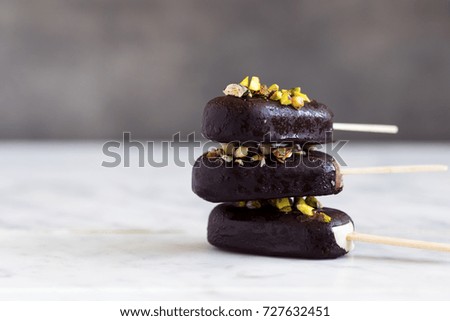 Chocolate glazed and pistachios popsicle ice-creams on concrete background. Copy space