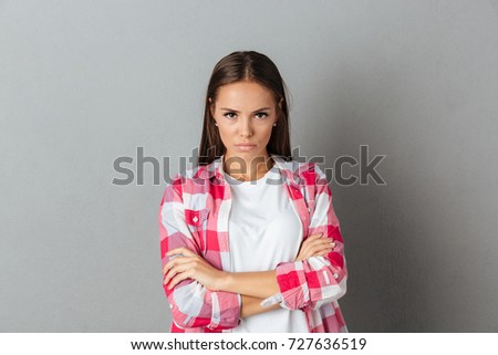 Photo of beautiful serious woman in checkered shirt standing with arms folded isolated over gray background