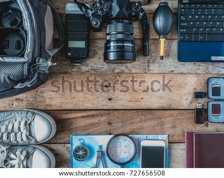 top view of photographer concept with digital camera, memory card, camera bag, lens, laptop, travel accessories, outfit of traveler on wooden background with copy space.