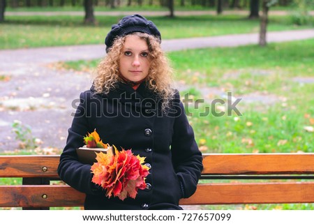 Girl in a black coat holding maple leaves and a book in the park in autumn