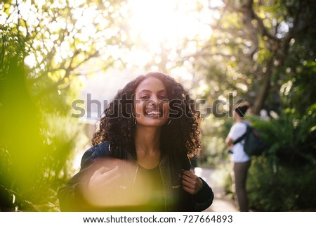 Closeup of curly haired woman standing in park with evening sun in the background.