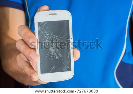 A young man holding a broken smart phone with a cracked screen