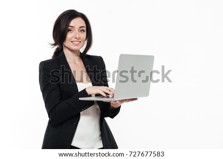 Portrait of a happy smiling businesswoman in a suit typing on laptop computer and looking at camera isolated over white background