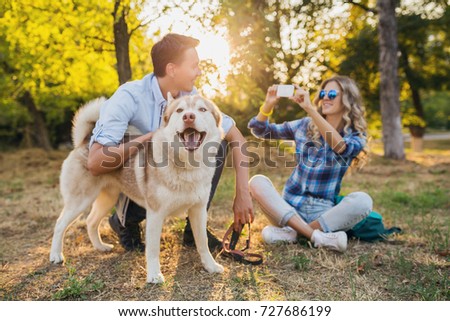 young hipster couple walking in park with husky dog, having fun, smiling, sunny weather, happy together, casual style, taking photo picture using phone