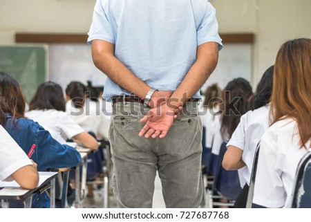 School exam room with teacher (invigilator) watching over students having stress studying in class or monitoring candidates taking examination in classroom for admission test education concept Royalty-Free Stock Photo #727687768