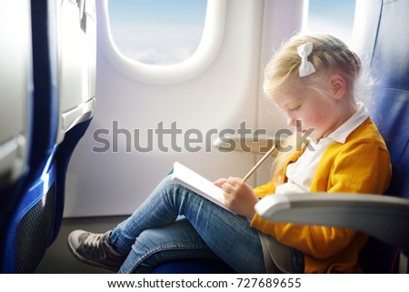 Adorable little girl traveling by an airplane. Child sitting by aircraft window and drawing a picture with colorful pencils. Traveling abroad with kids.