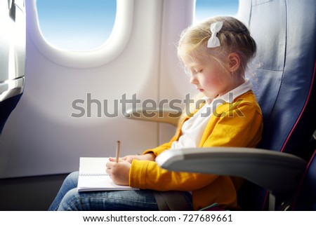 Adorable little girl traveling by an airplane. Child sitting by aircraft window and drawing a picture with colorful pencils. Traveling abroad with kids.