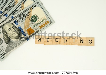 The word WEDDING spelled out in wooden alphabet tiles on an isolated white background. Hundred dollar bills pictured for concept weddings are expensive