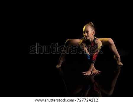 A young girl athlete gymnast performs acrobatic elements on a black background in a yellow scenic light.