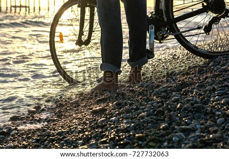 The legs of a man who stands with a bicycle along the seashore. Men's legs in jeans stands with bike at the sea, close up
