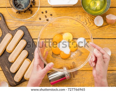 Photo on top of table with savoyardi cookies, hands with cup of eggs, coffee