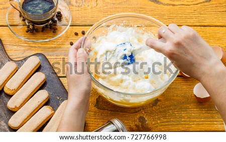 Picture of cooking tiramisu, human hands with culinary trowel , cookies, coffee, cups, cheese on wooden table