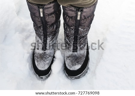 Human legs wearing warm snow boots standing on the snow, outdoor cropped photo