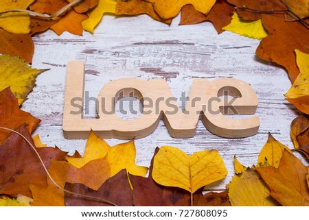 Wooden love sign on shabby white wooden background, with yellow leaves. Autumn concept. Top view.