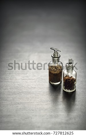 Two little bottles filled with cloves and caraway on grey table background