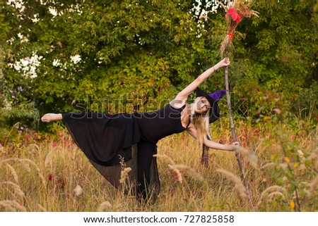 Young girl in Halloween witch costume practicing yoga positions with broomstick in her hands