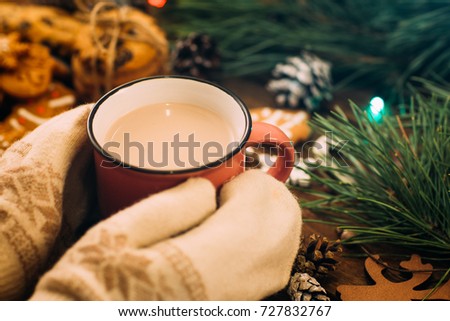 Warm Christmas holiday with latte and cookies. Close up unrecognizable woman with cup of drink in knitted gloves hands on festive background. Cozy xmas evening on festival and fairs concept