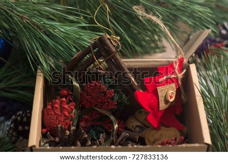 Festive box with decoration. Colorful strobilas, felt fir tree with sweet cookies and handmade wooden frame gathering in carton, close up picture. New Year and Christmas traditions and decor concept