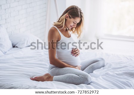Attractive pregnant woman is sitting in bed and holding her belly. Last months of pregnancy. Royalty-Free Stock Photo #727852972