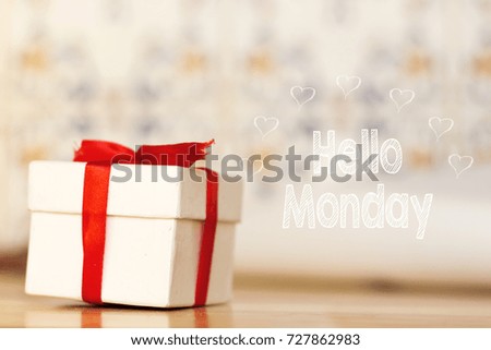 hello monday message with white gift box with red ribbon on wood background 