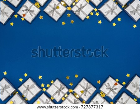 Border of silver shiny gifts and golden stars on blue background. New Year's and Christmas decorations. Group of bright gift boxes. View from above