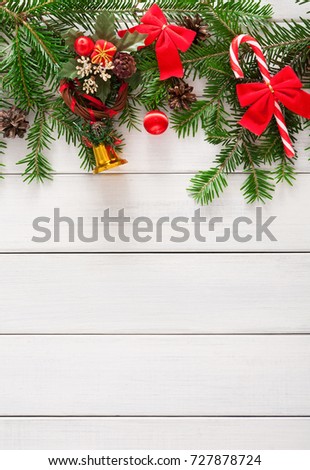 Xmas decoration, garland frame concept background, top view with copy space on white wooden surface. Christmas ornaments border with fir tree branches, bows, lollipop and bells