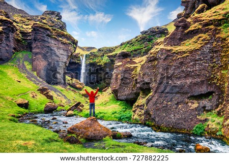 Colorful morning view of Kvernufoss waterfall. Picturesque scene in south Iceland with tourist standing on the rock. Traveling concept background.
