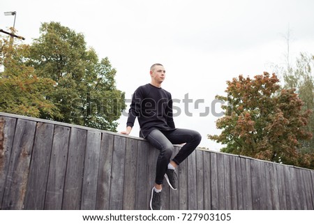 slender man walks in autumn Park. street style in clothes: black jeans and jacket. emotional portrait. short hair and troubled skin
