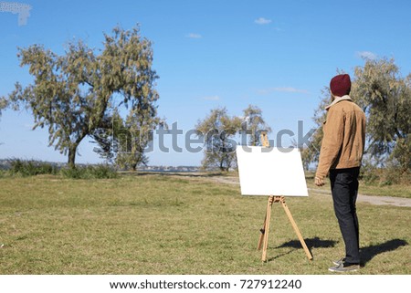 Young artist painting an autumn landscape on the nature background. Art concept.