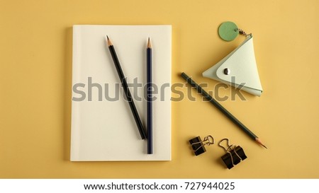 Copy space of top view empty book note, coin purse , paper clip and pencil on yellow paper background