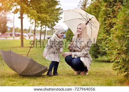 Young beautiful mom and her daughter wearing beige raincoats with umbrellas, autumn fashion style, fall family same look, clothing for parent and child.