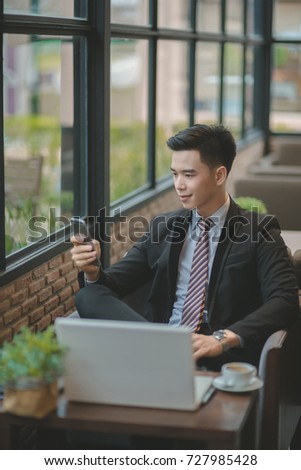 Happy  businessman using cellphone while sitting on sofa at his modern home.Concept of young people working on mobile devices.Blurred background