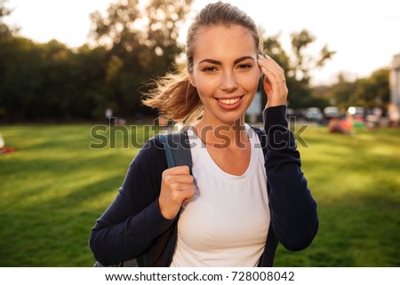 Close up portrait of a smiling happy girl student standing with backpack and looking at camera outdoors