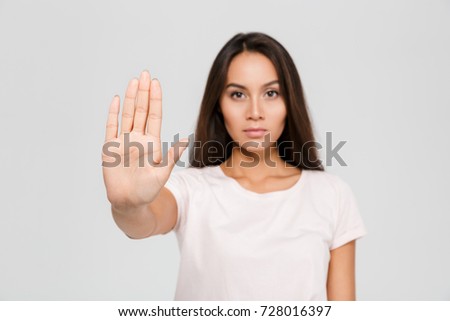 Portrait of a serious young asian woman standing with outstretched hand showing stop gesture isolated over white background, focus on hand