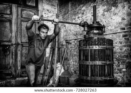 Shirtless winemaker farmer working on a traditional wine press. Black and white picture