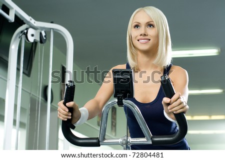 happy cutie athletic girl ,  execute exercise on exercise bicycle  and smile, in  sport-hall