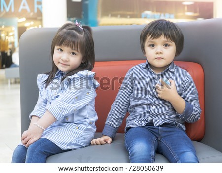 Cute little boy and beautiful little girl hugging and sitting on sofa, Happy two toddler sitting together after playing around, Friendship concept
