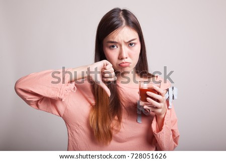 Young Asian woman  thumbs down hate tomato juice on gray background