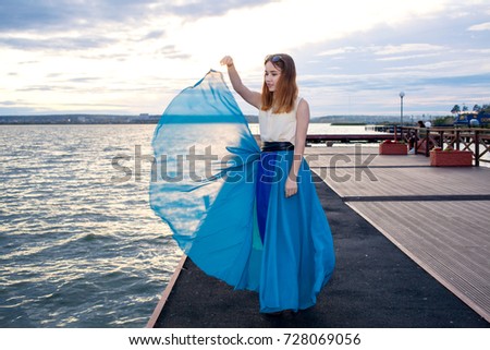 Girl in a dress by the sea at sunset dances