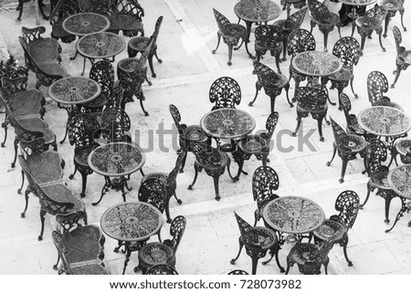 Openwork chairs and tables in a street cafe on Malta. Black and white picture