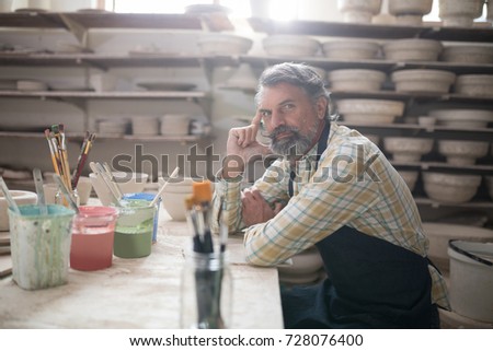 Portrait of male potter sitting at worktop in pottery workshop