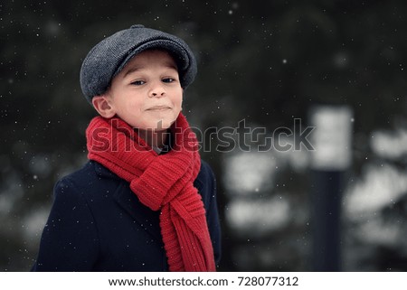 Portrait of a cute little boy in red scarf and cap. Image with selective focus and toning.