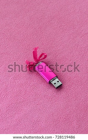 Brilliant pink usb flash memory card with a pink bow lies on a blanket of soft and furry light pink fleece fabric. Classic female gift design for a memory card