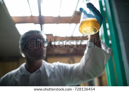 Low angle view of scientist examining beer in beaker at doorway in factory