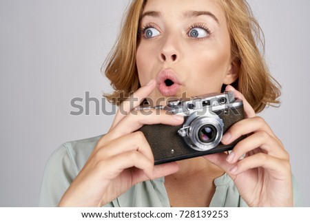 surprised young woman photographer holding a camera on a gray background portrait                               