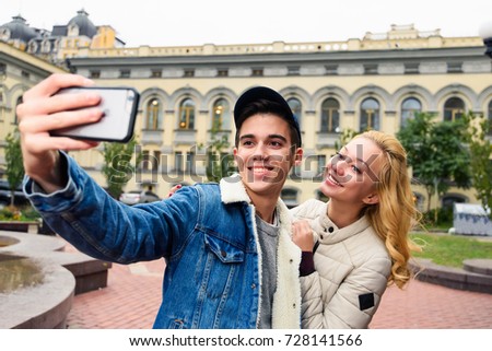 Young smiling couple taking a selfie with smartphone while walking through the city. Happy tourists enjoy their travel holidays.  