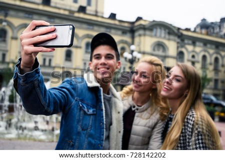 Friendship, travel, technology and people concept - group of smiling friends with smartphone making selfie against the background of touristic attractions. Focus on the phone.