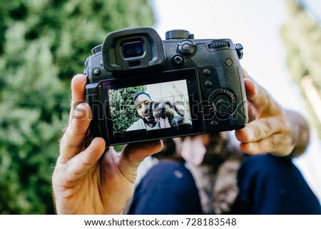 
Young man enjoying a sunny day in the park with his brown dog. They are taking a picture together with the camera. Lifestyle